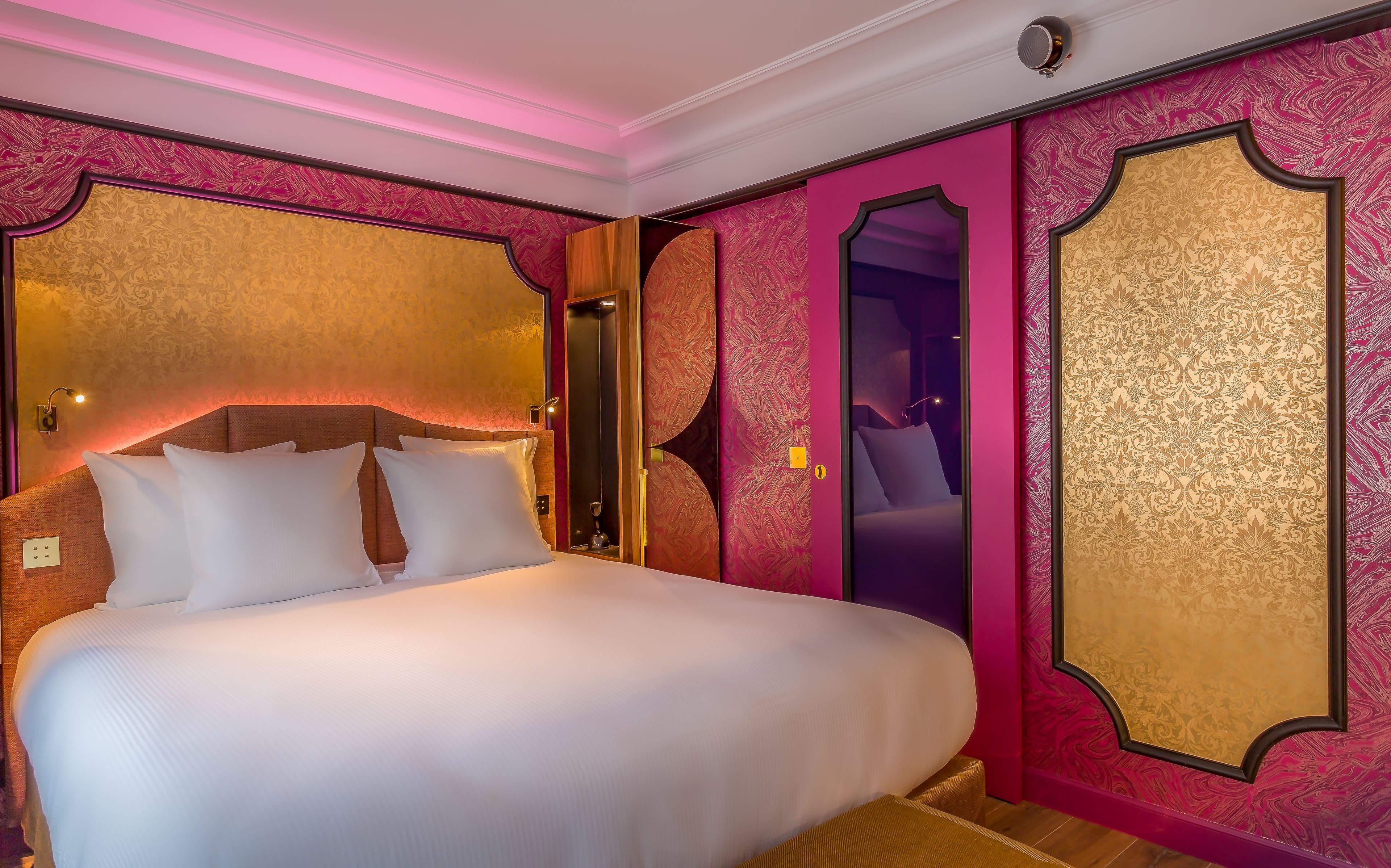 A large bed with white linens in a room with ornate gold and pink wallpaper.