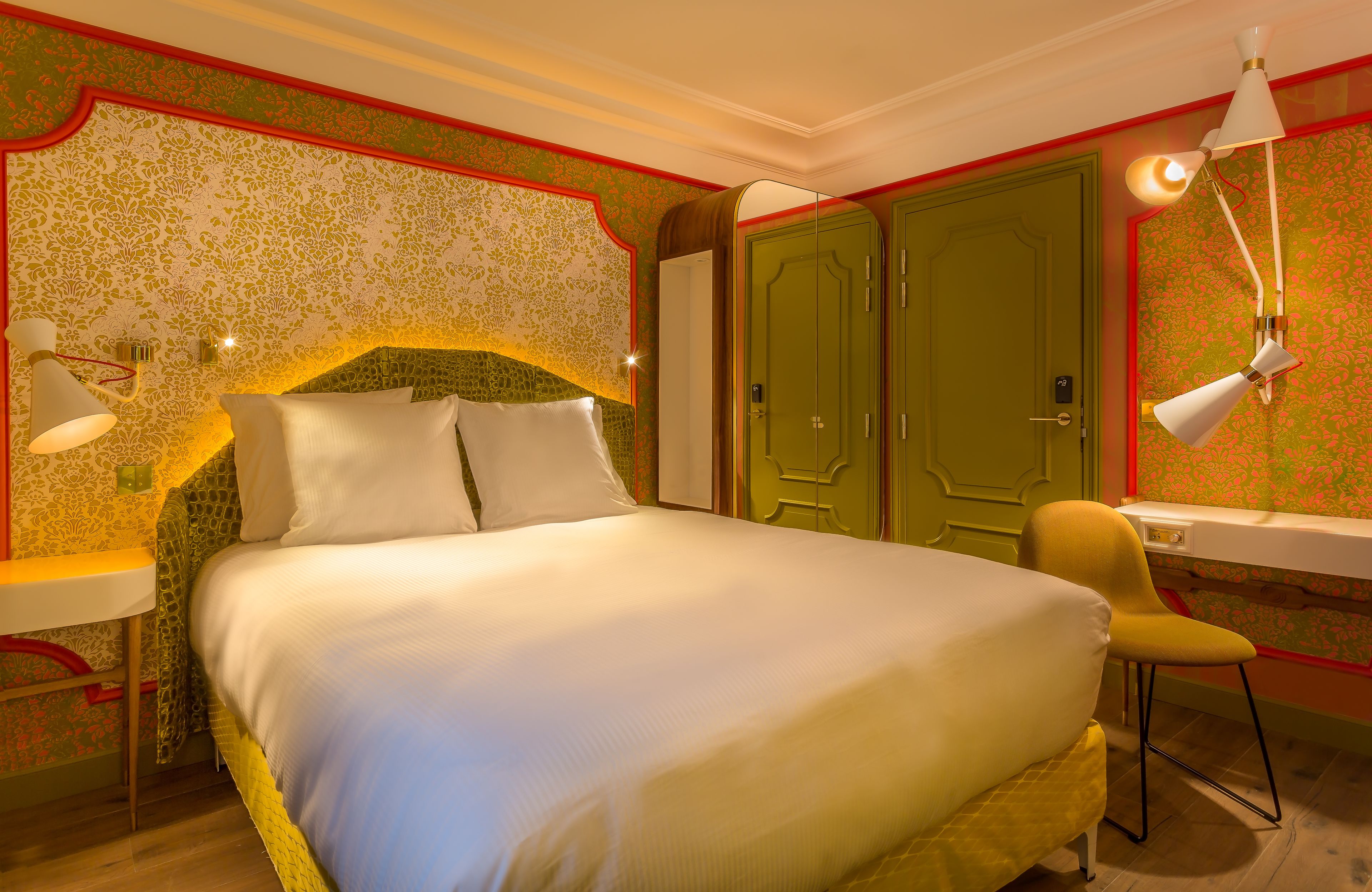 A neatly made bed with pillows, a bedside lamp, a chair, and a wardrobe with a mirror.