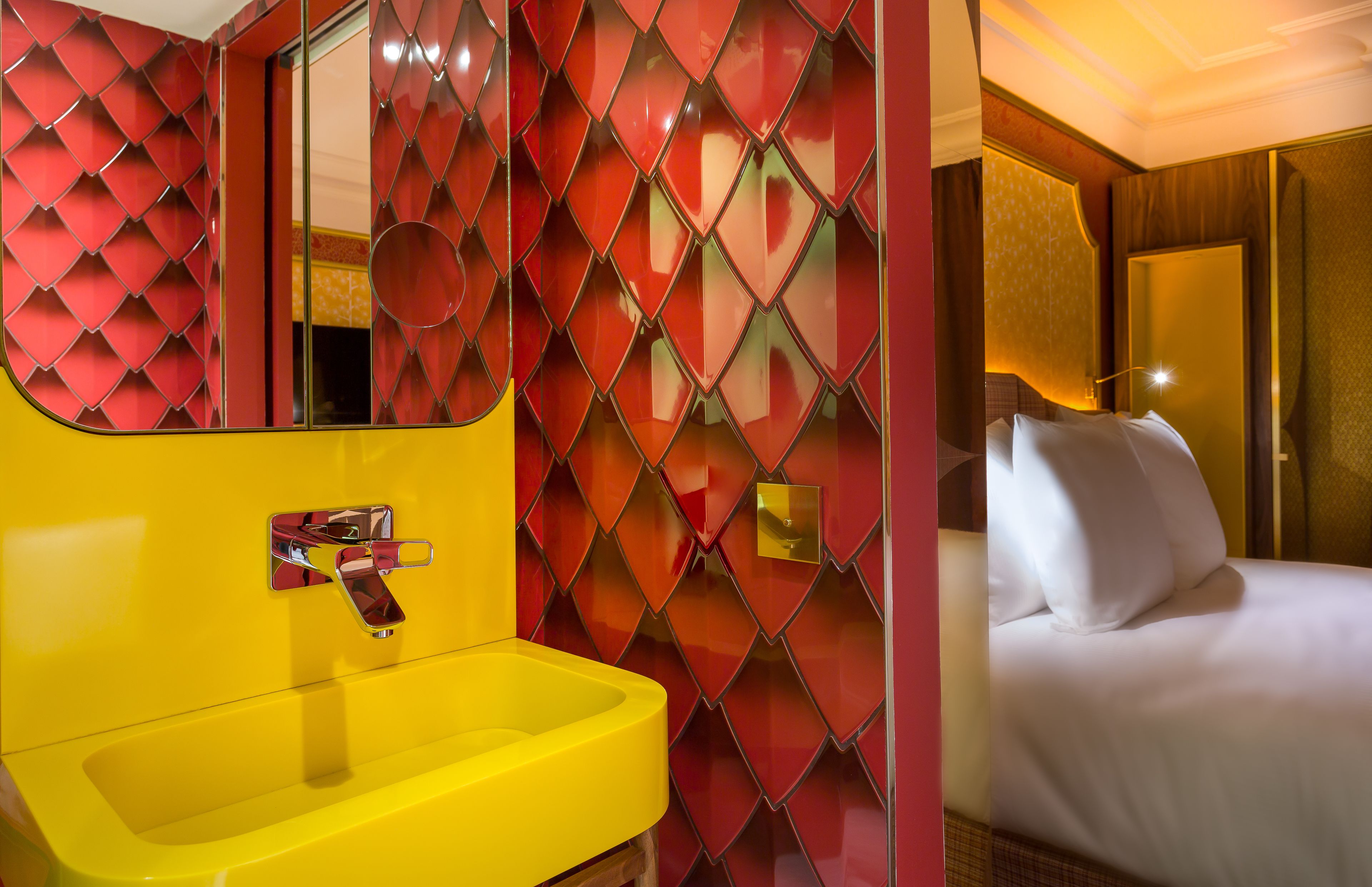 A hotel room with a yellow sink, a bed with white bedding, and a red patterned wall.