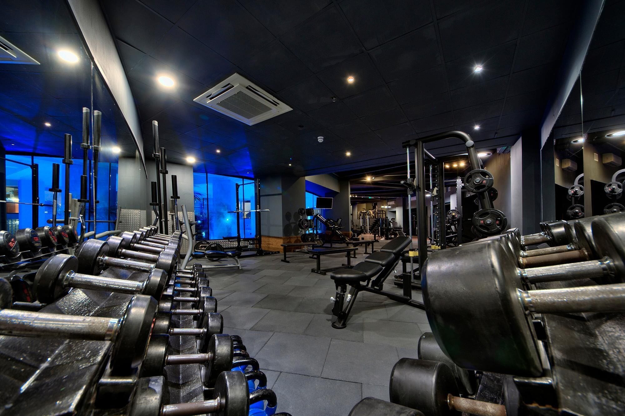 A gym with various weightlifting equipment, benches, and a mirrored wall.