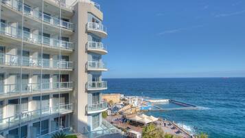 A multi-story hotel with balconies overlooking the sea, a dock area with boats, and a clear view of the ocean.
