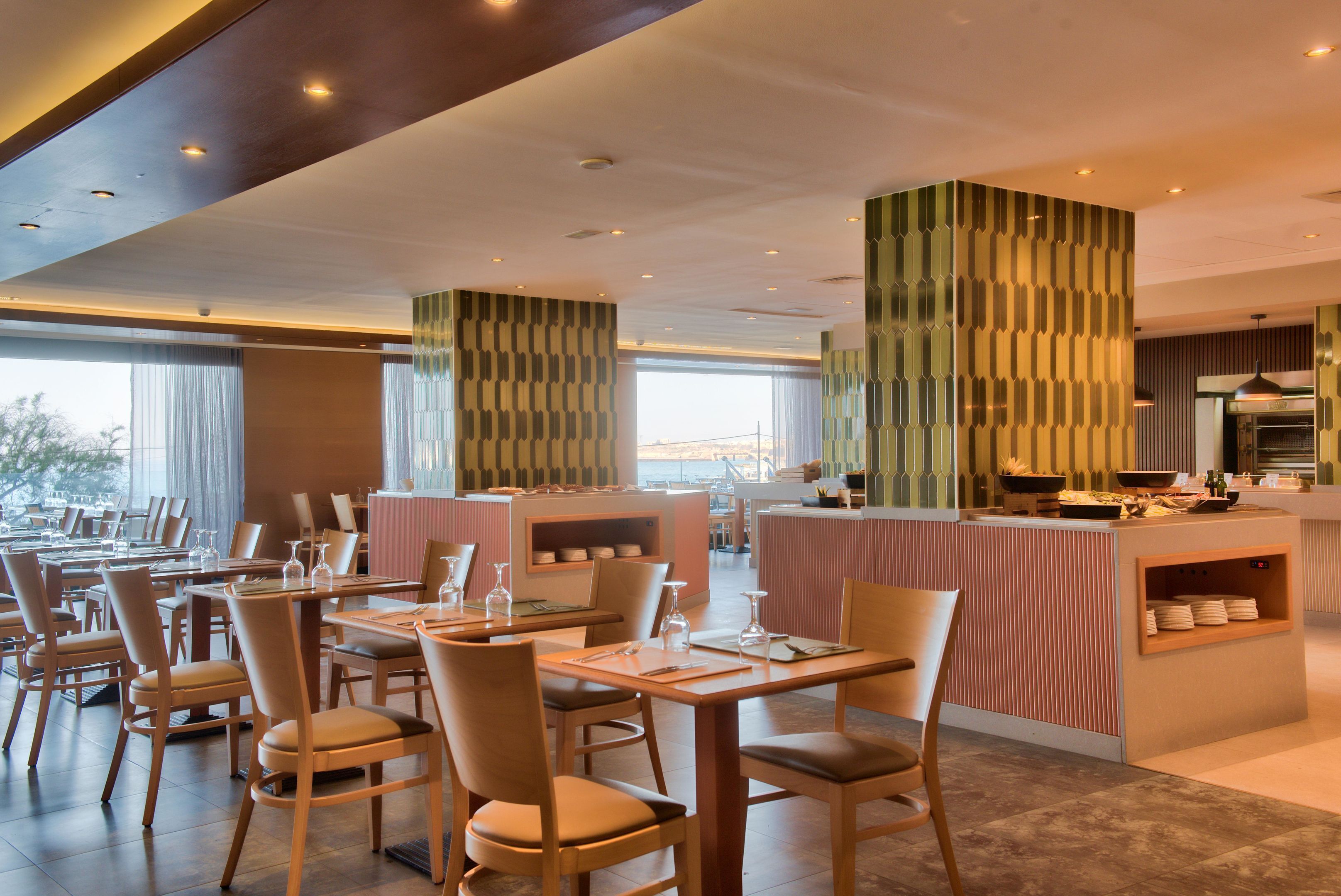 A modern restaurant with wooden tables and chairs, a central counter, and a view of the outdoors.