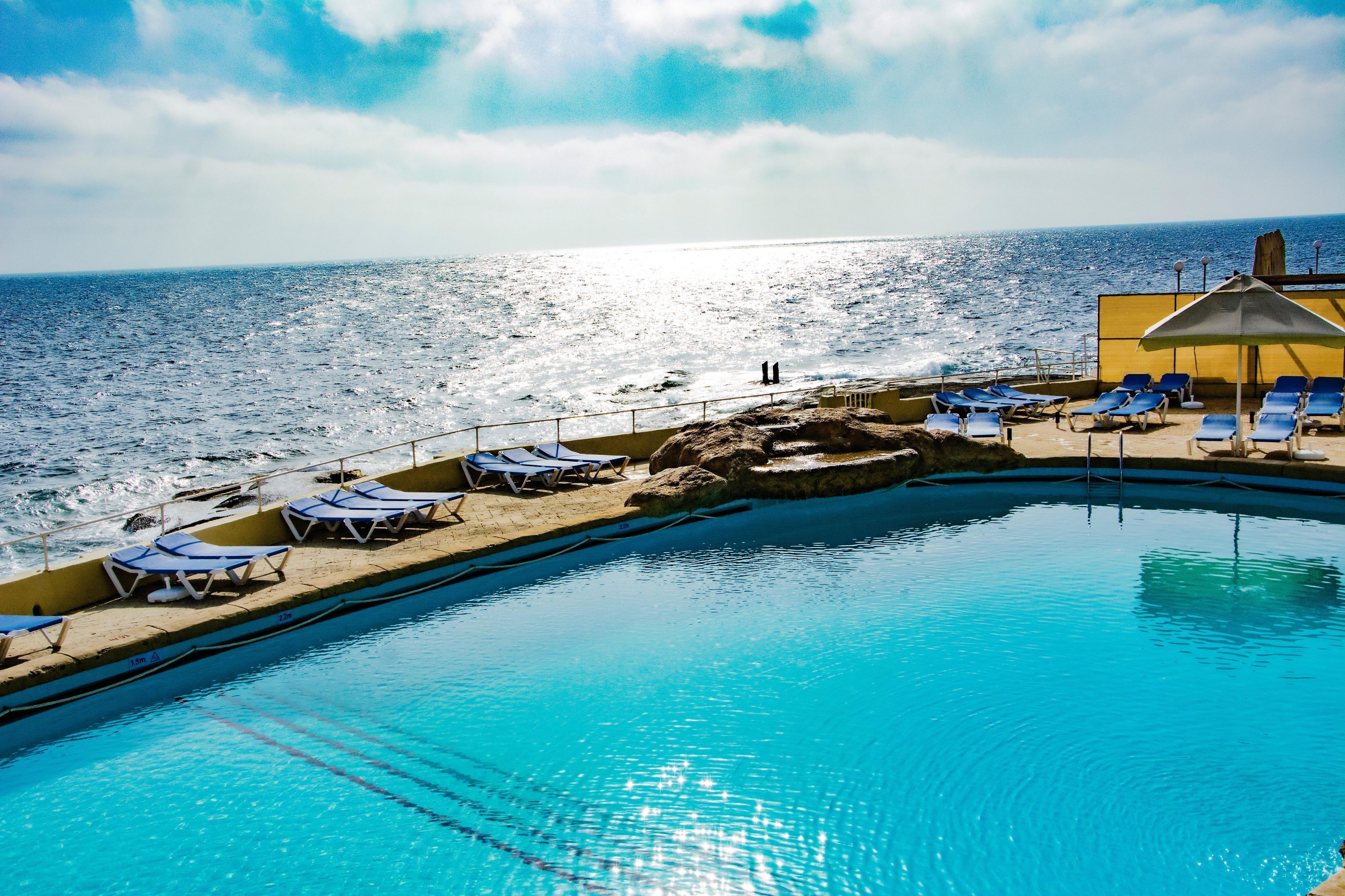 Una piscina con acque cristalline, circondata da lettini e vista sull'oceano.