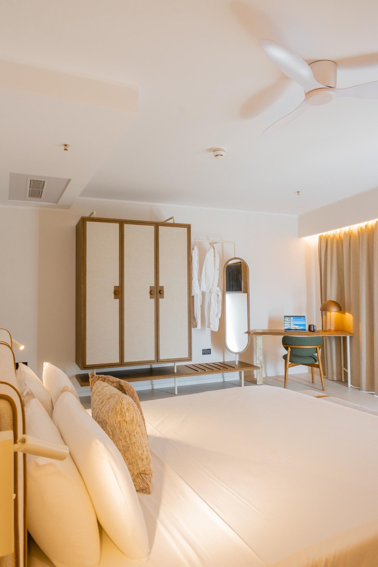 Habitación de hotel con una cama grande, un escritorio con computadora, una silla, un armario y un ventilador de techo.