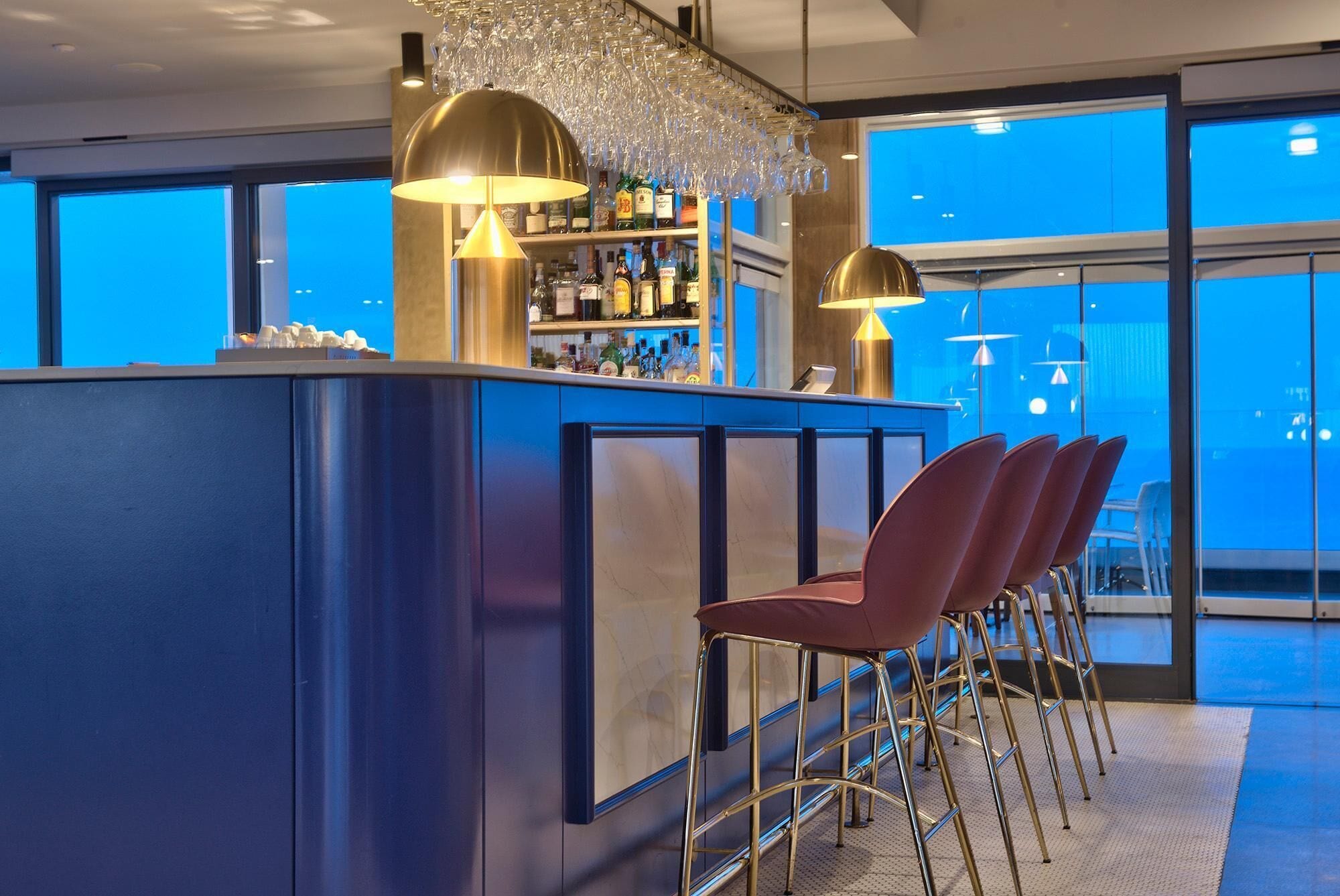 Un área de bar moderna con una barra azul, lámparas colgantes doradas y taburetes rojos.
