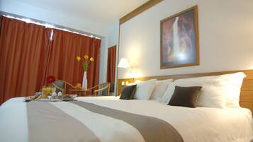 Habitación de hotel con una cama grande, una mesa de comedor con alimentos para el desayuno, una silla y un cuadro en la pared.