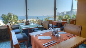 A restaurant with tables set for dining, featuring a view of the sea and buildings in the background. - The Preluna Hotel (Sliema)