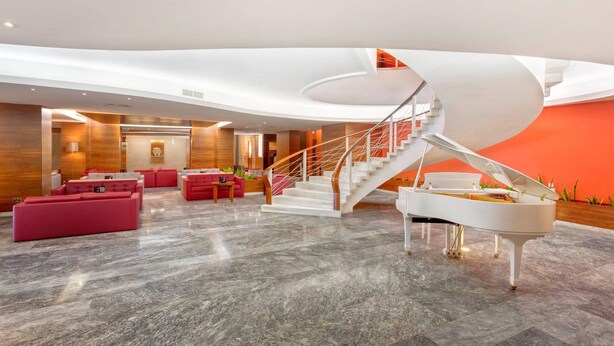 A modern lobby with a grand piano, red seating, and a unique spiral staircase. - The Preluna Hotel (Sliema)