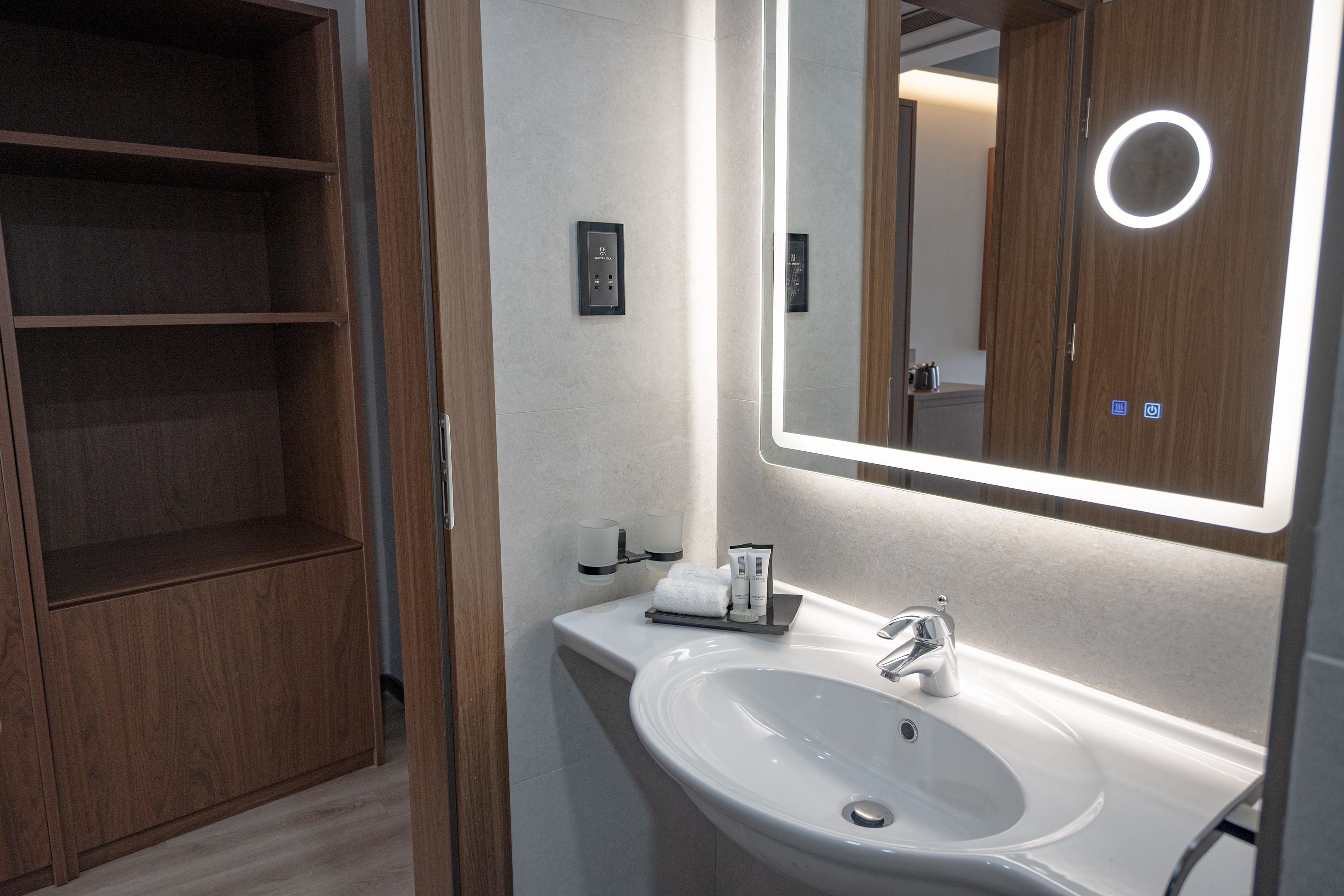 A modern bathroom with a white sink, mirror, and wooden shelving.