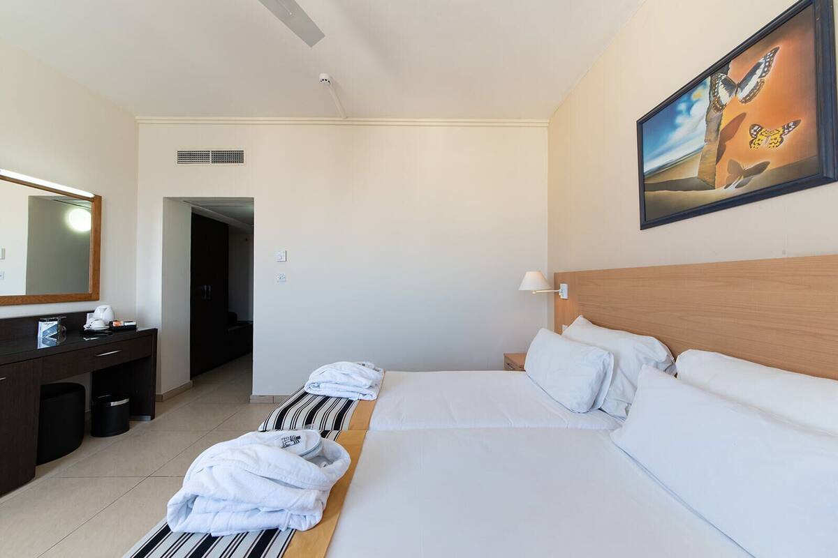 Habitación de hotel con una cama, un escritorio, una silla, un espejo y un cuadro en la pared.