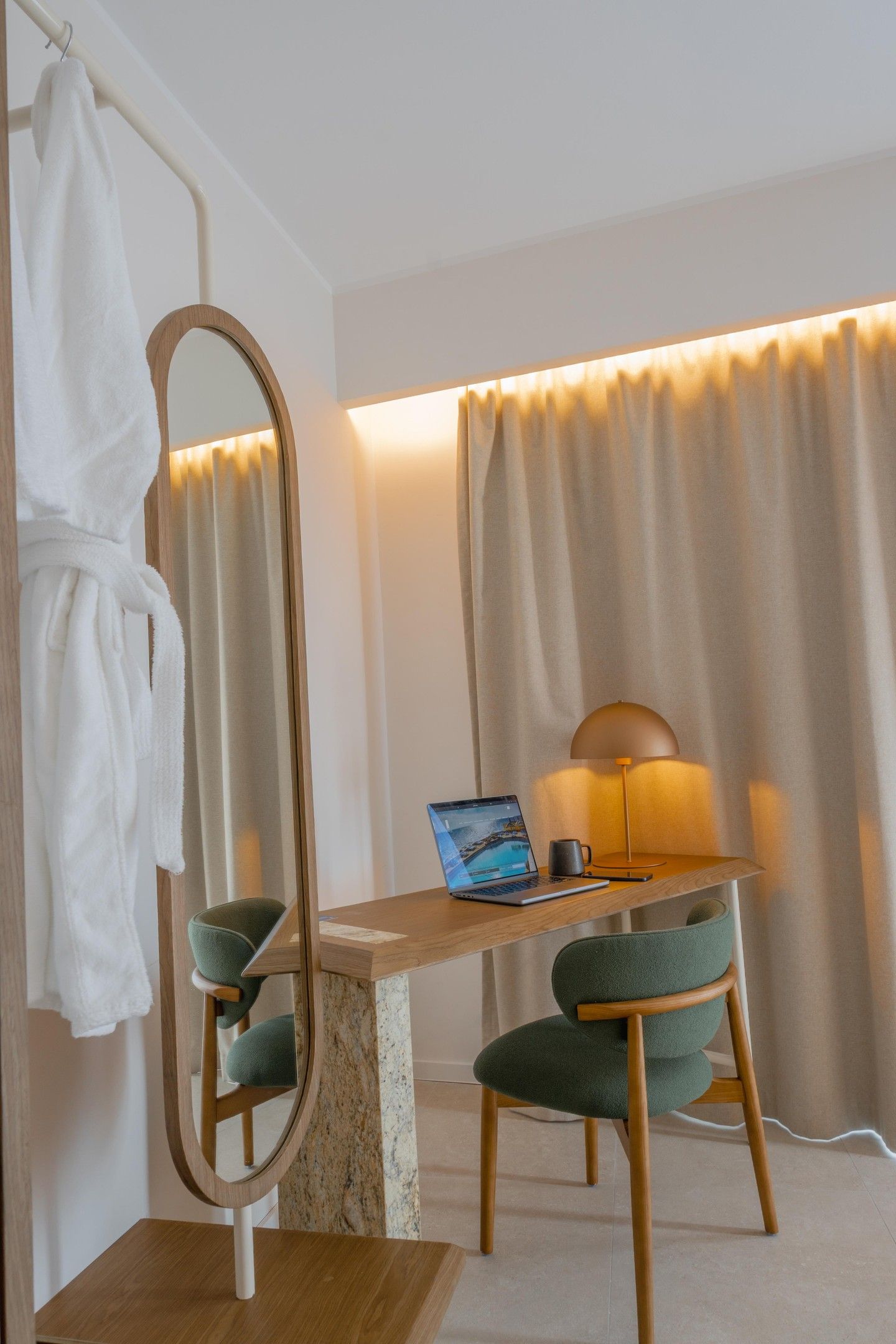 Una camera d'albergo con una scrivania in legno, un computer portatile, una lampada e uno specchio.