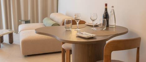 A modern dining area with a round wooden table, two chairs, and a sofa in the background.