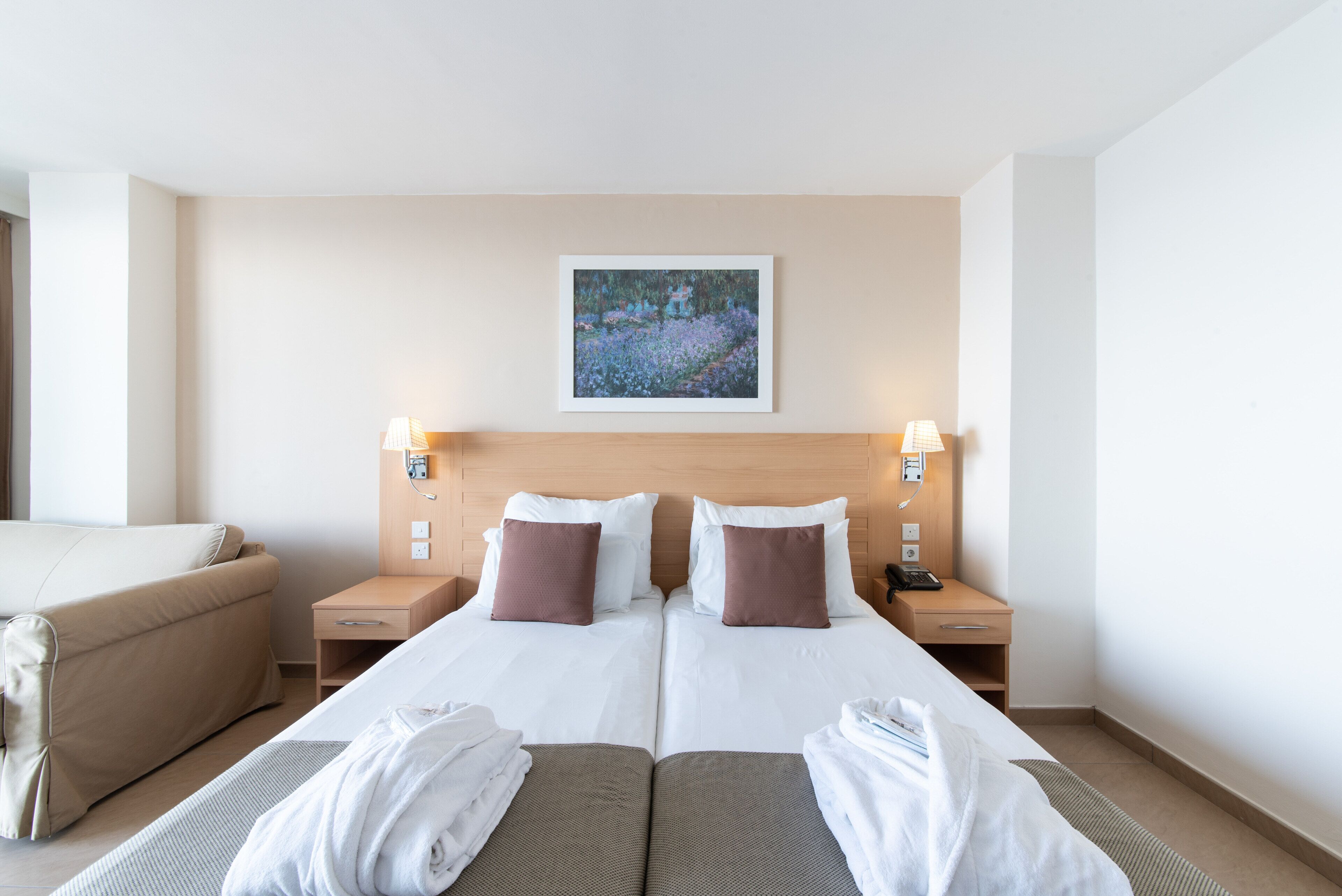 Hotelkamer met een tweepersoonsbed, twee nachtkastjes, een lamp, een schilderij aan de muur en een bank.