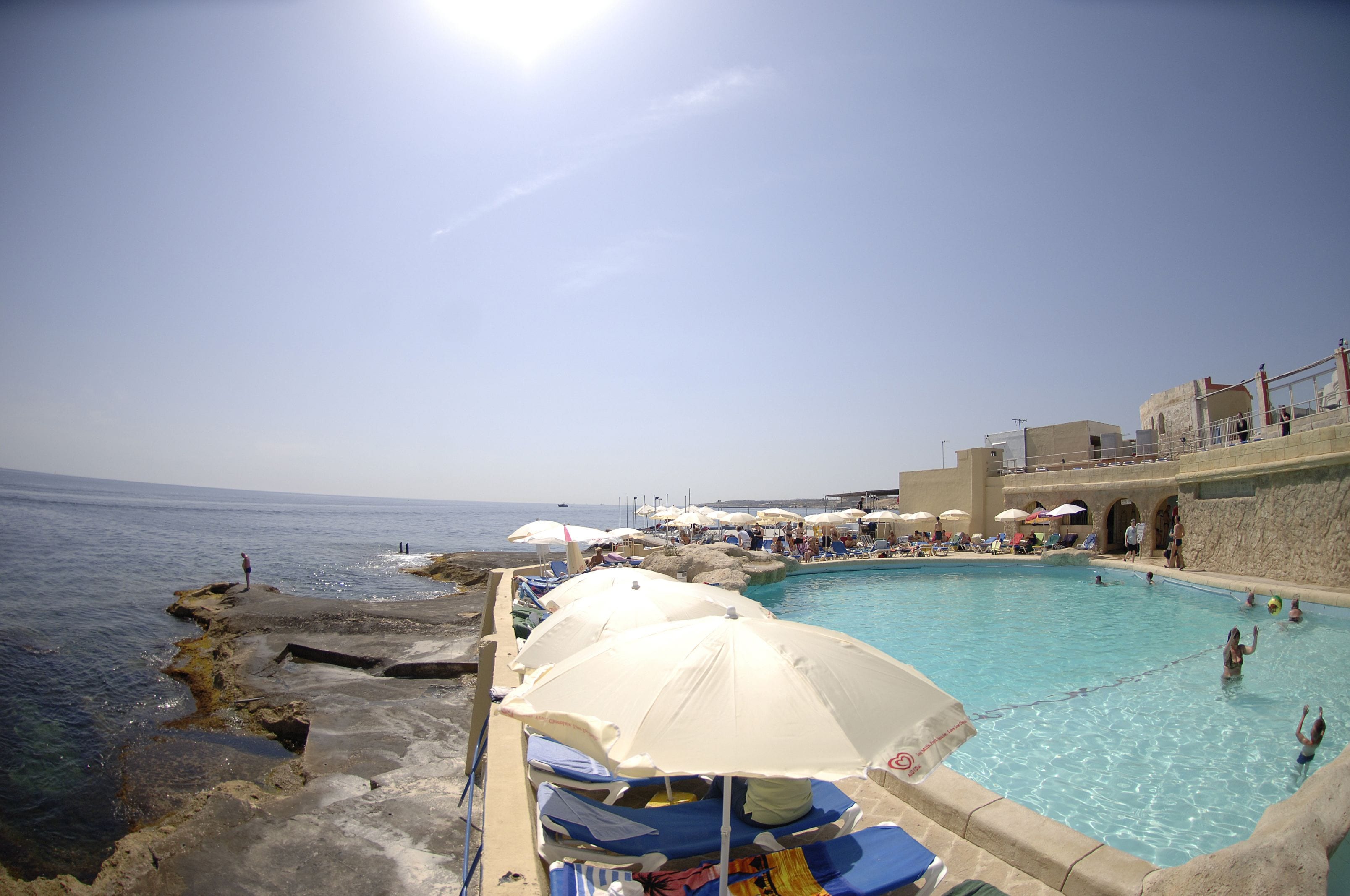 A pool area with umbrellas, lounge chairs, and a view of the sea.
