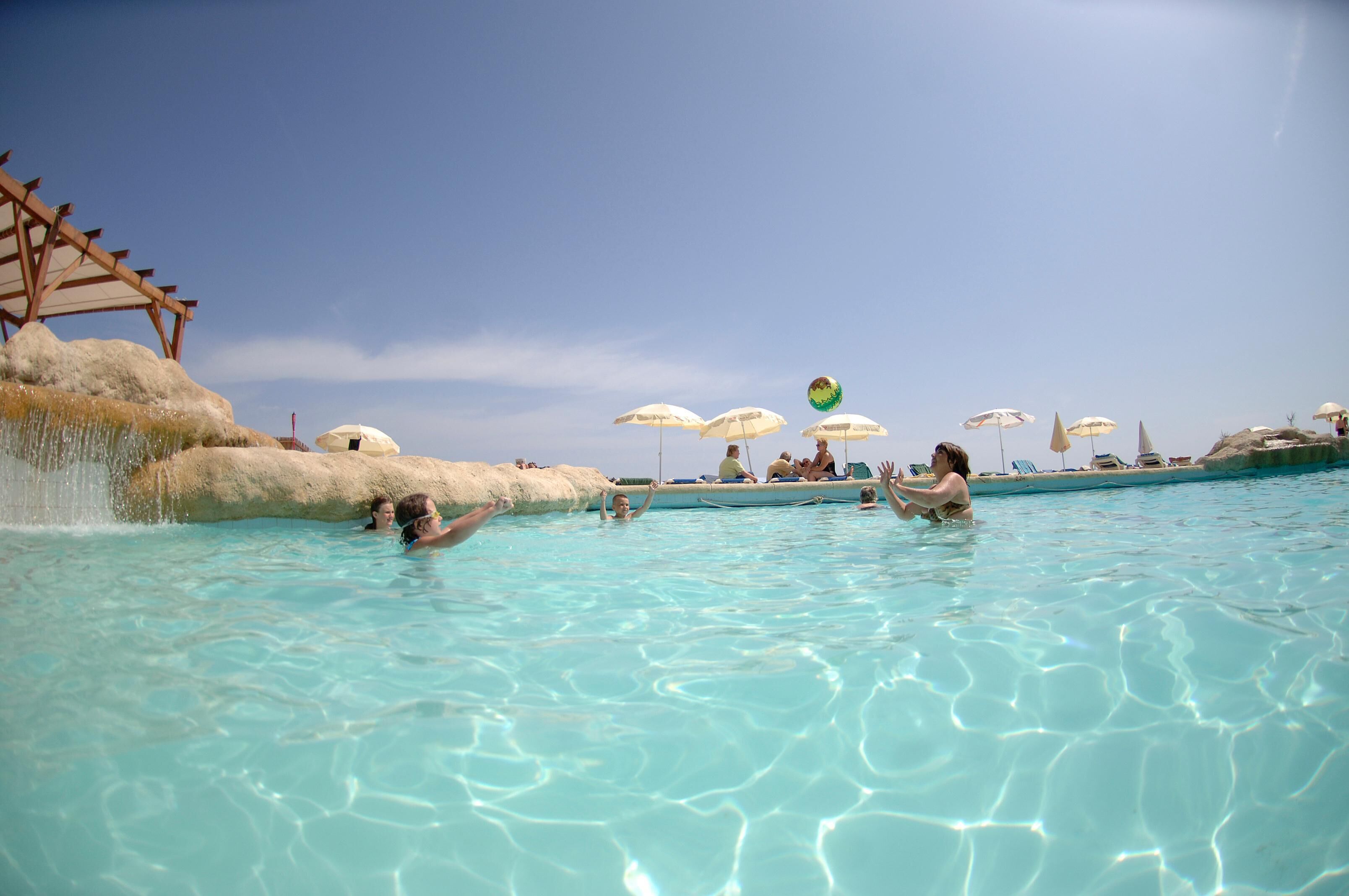 Ein Schwimmbecken mit klarem Wasser, Sonnenschirmen und einer Felsformation.