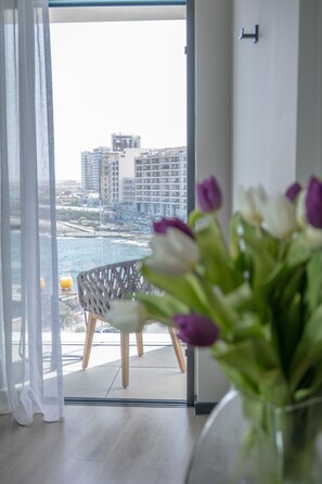 A room with a view of the sea and buildings, a chair, and a vase with flowers. - The Preluna Hotel (Sliema)