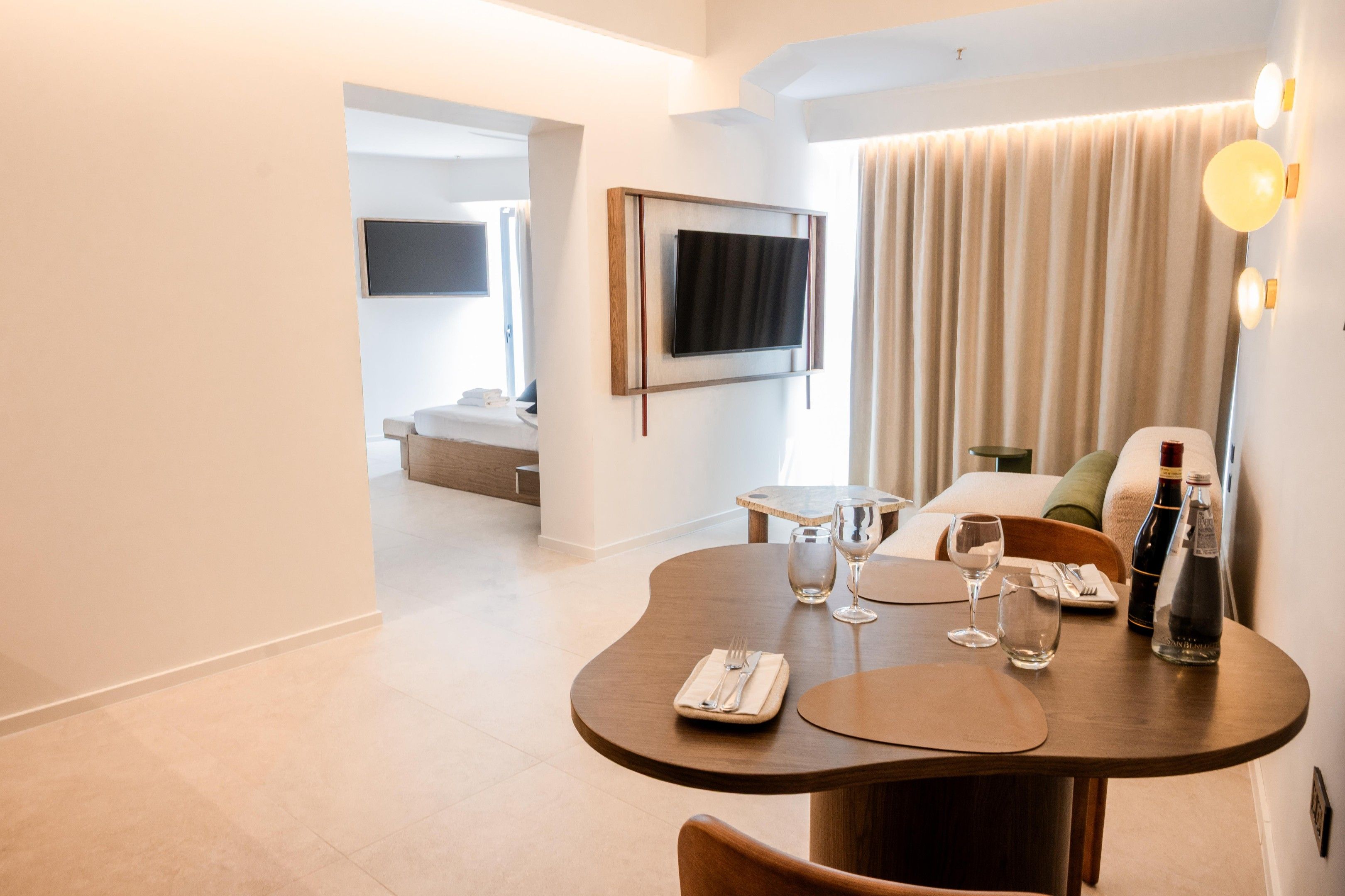 Ein modernes Hotelzimmer mit Essbereich, einem flachbildfernseher an der Wand und einem großen Fenster mit Vorhängen.