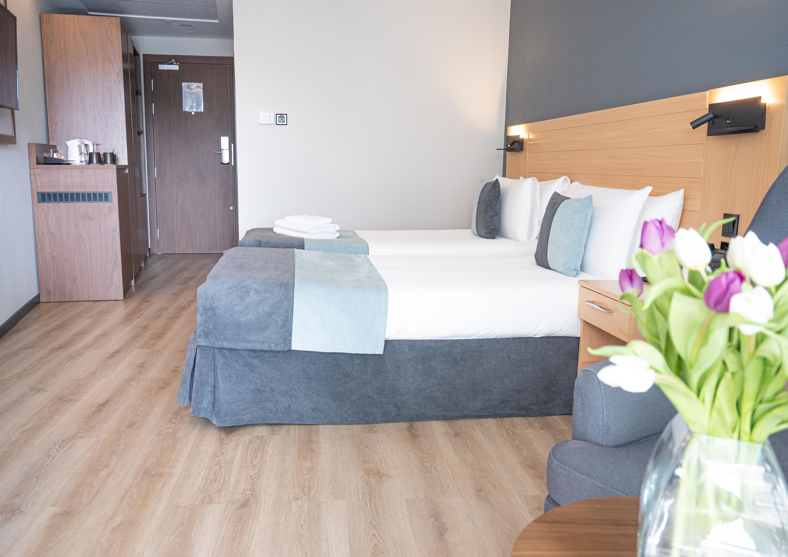 A hotel room with a bed, bedside table, and a small kitchenette.