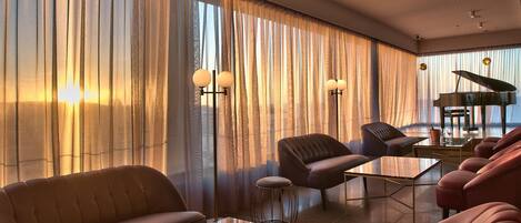 A modern living room with a piano, leather sofas, and a large window with sheer curtains.