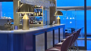 A modern bar area with a bar counter, two pendant lights, and a row of bar stools. - The Preluna Hotel (Sliema)