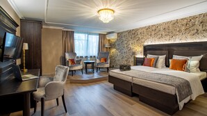 Habitación de hotel con una cama grande, un escritorio con una computadora portátil, dos sillones, una mesita y un televisor.