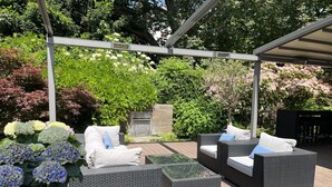 Un patio exterior con mobiliario de mimbre, una pérgola y abundante vegetación.