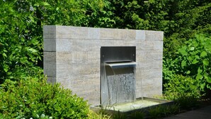 Una fuente exterior moderna con una estructura de piedra y un flujo de agua en cascada.
