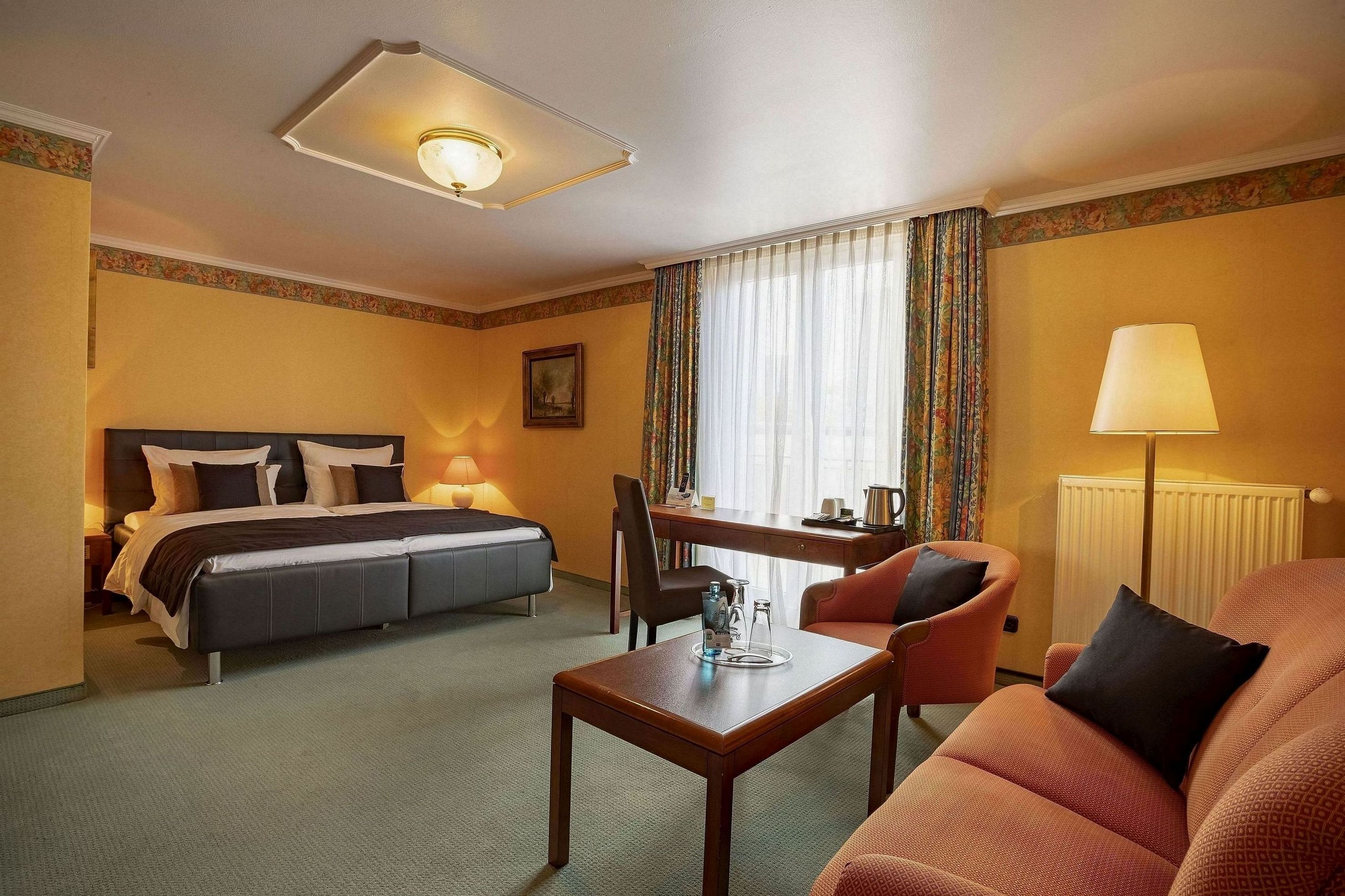 A hotel room with a bed, a desk, a chair, a sofa, and a lamp.