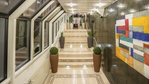 Un moderno vestíbulo de hotel con una escalera de mármol, plantas en macetas y una llamativa obra de arte abstracta en la pared.