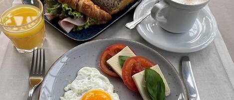 A breakfast setting with a croissant, bread, a plate with an egg, tomatoes, cheese, and olives, a glass of orange juice, and a cup of coffee.