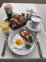 Un desayuno con un croissant, pan, un plato con huevo, tomates, queso y aceitunas, un vaso de zumo de naranja y una taza de café.