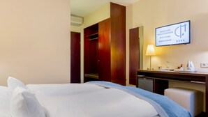A hotel room with a bed, a desk with a lamp, a television displaying a welcome message, and a wardrobe.