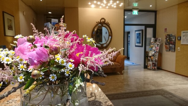 A reception area with a floral arrangement, a mirror, a couch, and a magazine rack.