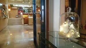 A hotel lobby with a glass display case containing a decorative item. There are wooden floors, a staircase, and a reception area in the background.