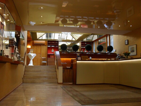 Un vestíbulo de hotel con mostrador de recepción, escalera y zona de espera.