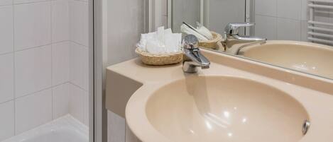 Une salle de bain avec un lavabo beige, un miroir et un panier en osier contenant des articles de toilette.