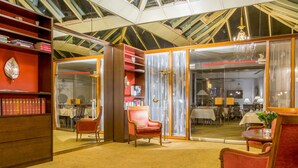 A spacious room with a high ceiling, a large window, and a chandelier. There are wooden bookshelves and a red armchair.