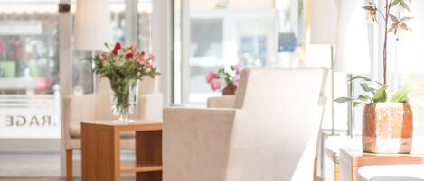 A modern interior with a beige armchair, wooden side tables, and potted plants.