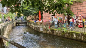 Un café a la orilla del río con terraza, un puente y un pequeño canal.