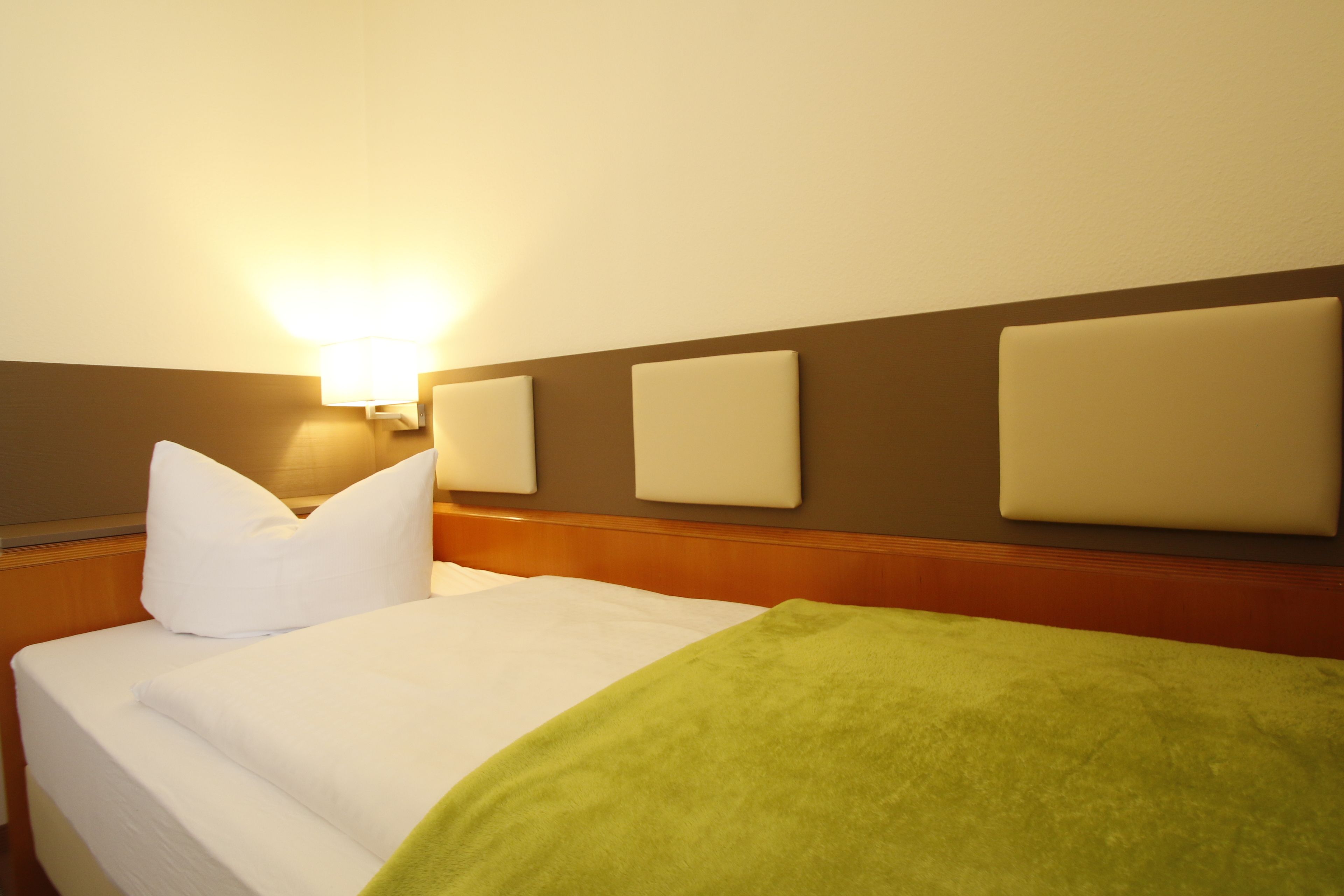 Una habitación de hotel con una cama, una mesita de noche y una lámpara fijada a la pared.