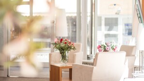 Una habitación de hotel moderna con un ventanal grande, un florero sobre una mesita auxiliar y una lámpara.