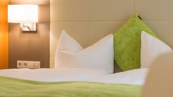 A hotel room with a bed, white pillows, a green pillow, a wall-mounted lamp, and a green throw blanket.