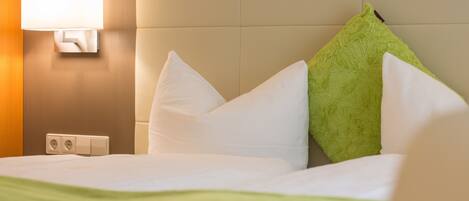 A hotel room with a bed, white pillows, a green pillow, a wall-mounted lamp, and a green throw blanket.