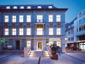 Un hotel con una entrada imponente, una escalera que conduce a las puertas principales y un letrero que dice “SORAT HOTEL”.