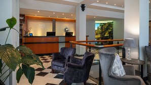 A hotel lobby with a reception desk, seating area, and a view of the outdoors. - Sorat Hotel Cottbus (Cottbus)