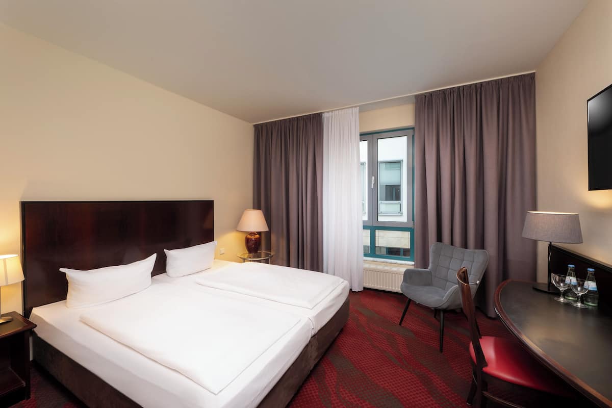 A hotel room with a large bed, a desk, a chair, and a TV.