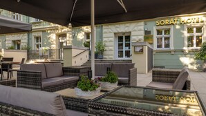 An outdoor seating area with wicker furniture and potted plants, a glass table, and a building with the sign "SORAT HOTEL". - Sorat Hotel Cottbus (Cottbus)