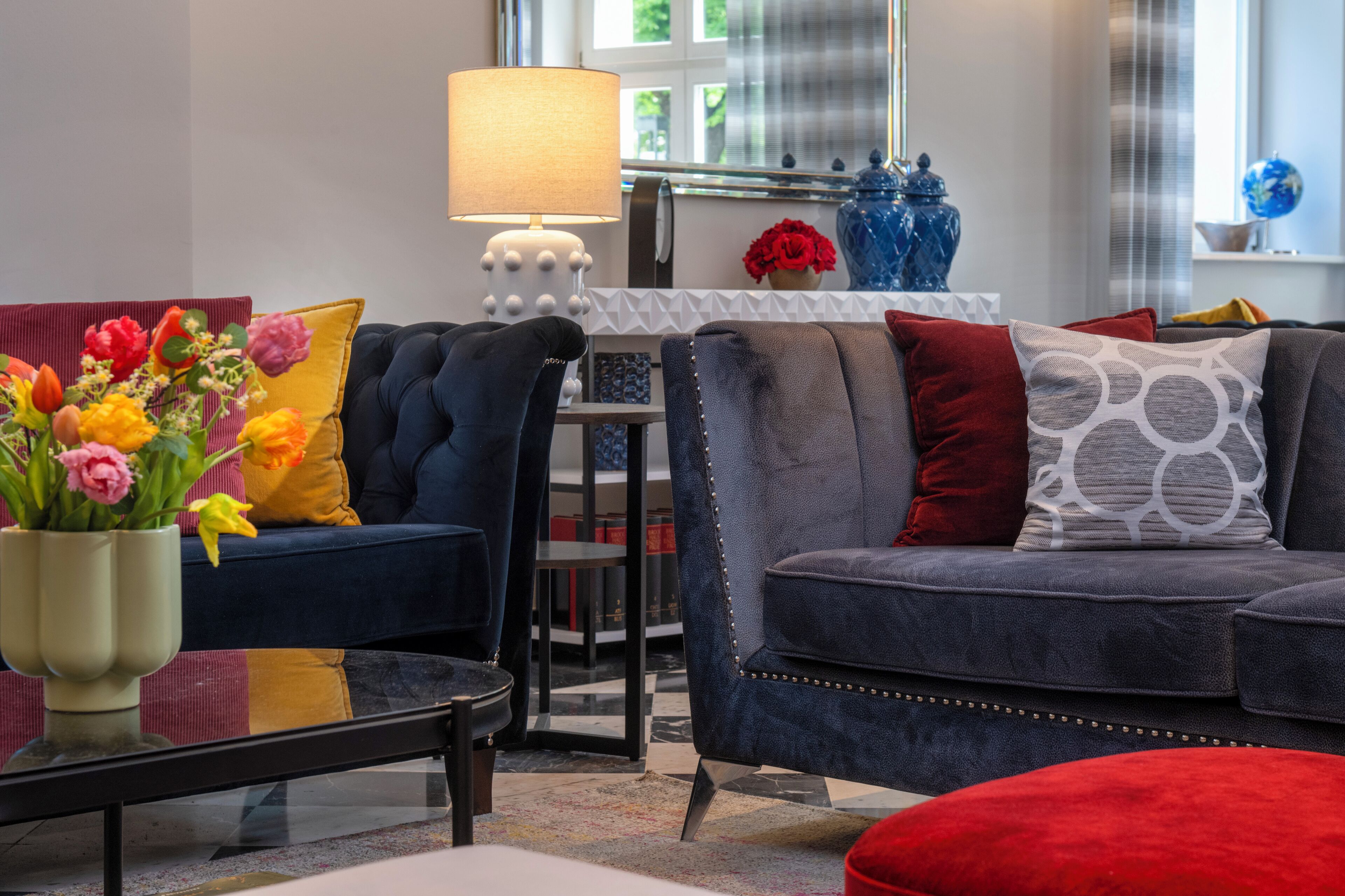 Un salon moderne avec un canapé bleu foncé, un pouf rouge et une table basse agrémentée d’un vase de fleurs.