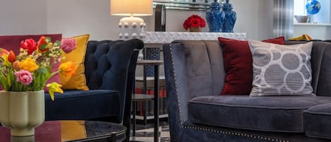 A modern living room with a dark blue sofa, a red ottoman, and a coffee table with a vase of flowers.