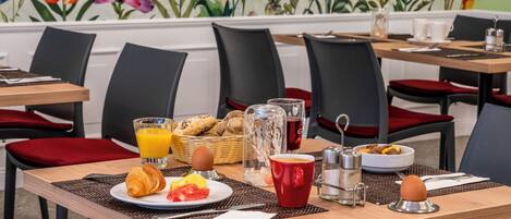 A breakfast setting with a table set for two, including croissants, fruit, and a coffee cup.